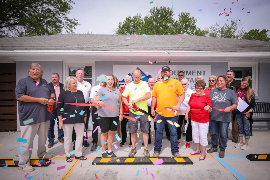 Multicolored confetti continues to blow in front of the camera while staff cut the ribbon with giant red scissors.