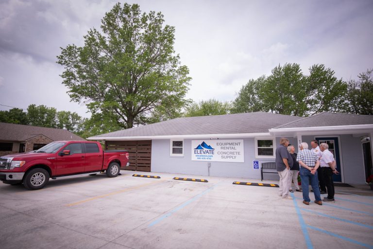 The facade of Elevate Equipment & Concrete Rental. The building is a grey, one story property with a white sign out front featuring their blue logo.