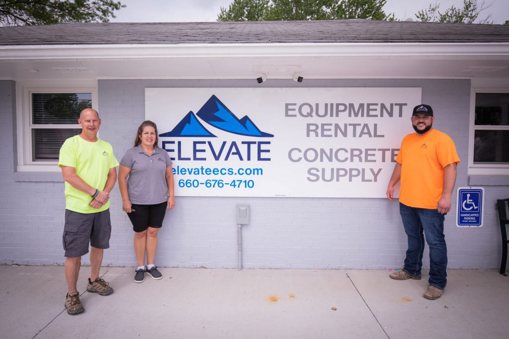 Three staff members stand beside the Elevate sign outside of their building.